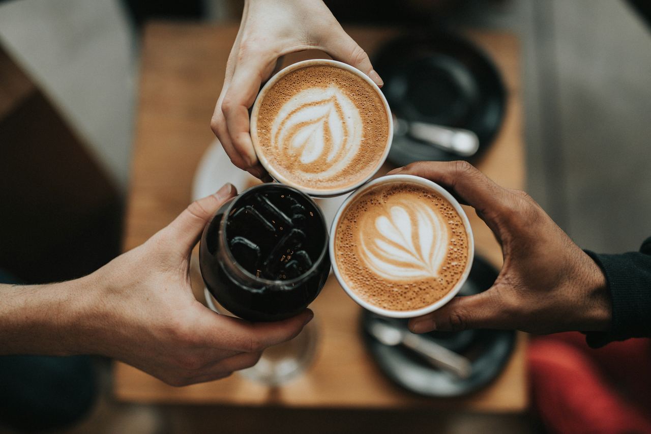 Trois personnes trinquent avec leurs tasses de café au-dessus d'une table.