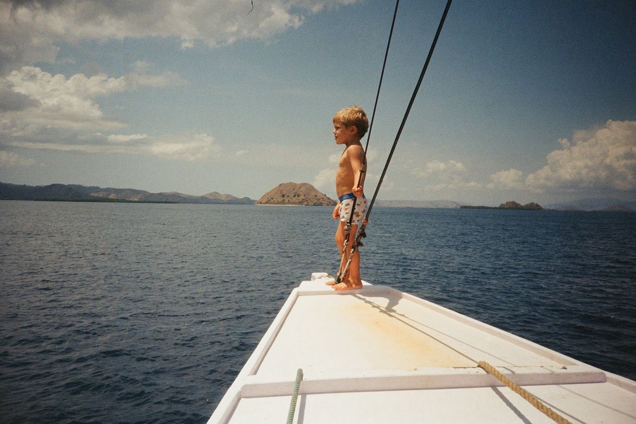 Un enfant debout à l'avant d'un bateau, regardant l'horizon.