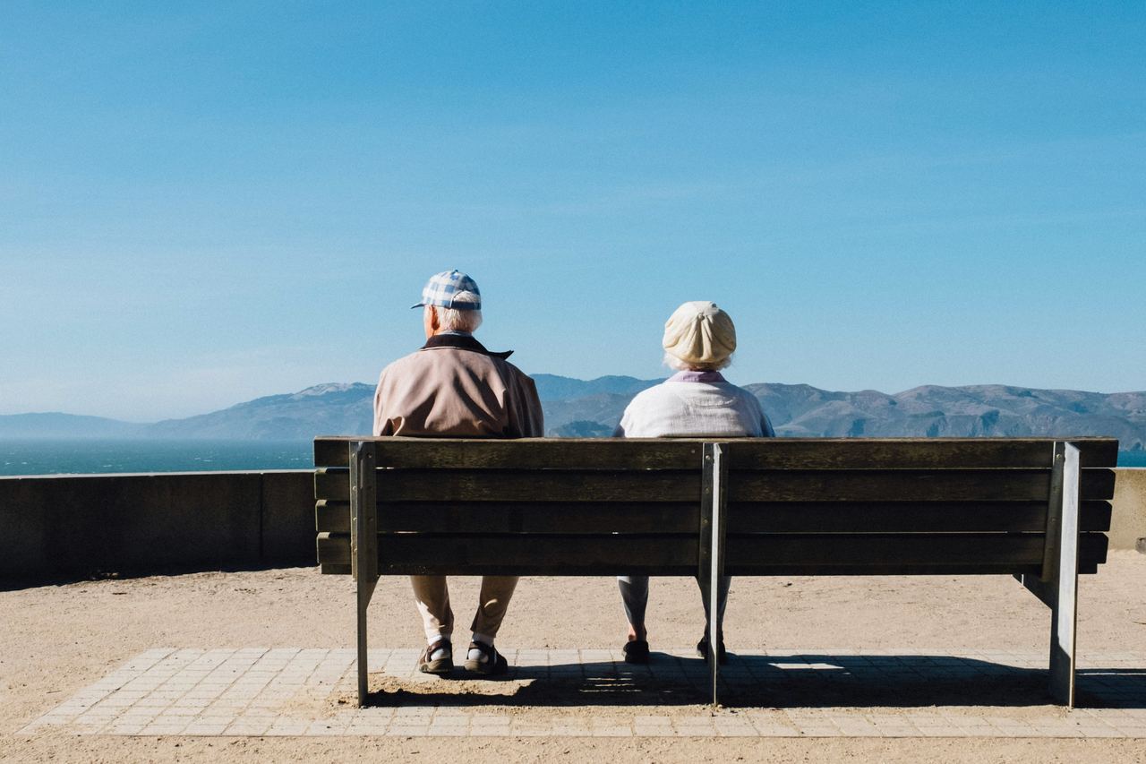 Un couple de personnes âgées assis de dos sur un banc, face à la mer.
